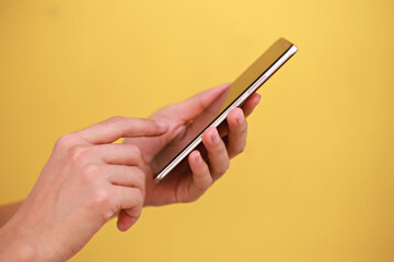 Female hand holding smartphone isolated on yellow background. 