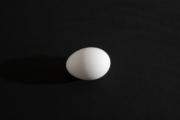 White egg on black background. Traditional symbol of food, kitchen, bakery and Easter.