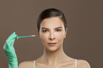 Pretty model woman with syringe injection near cheeks on brown background. Cosmetology and aesthetic surgery concept