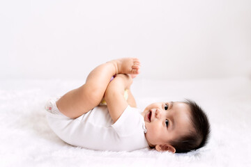 A cute 6 months old asian little baby boy is playing his hands and feet with fully happiness moment on the bed in the morning time, concept of healthy and child development in the first year of life.