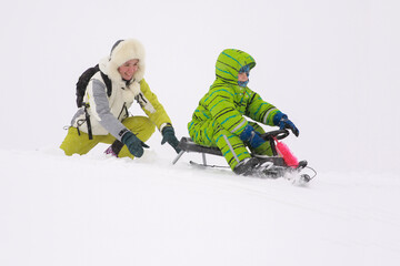 Fototapeta na wymiar Mom and son sledding from the mountain in winter in heavy snow
