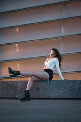 Lifestyle, a pretty brunette girl sitting in the city at the blue hour next to a gray building, wearing black boots and a short black skirt