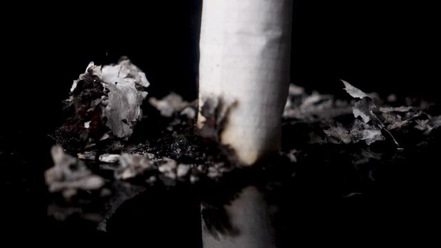 Macro stub out a cigarette on black surface in slow motion, isolated
