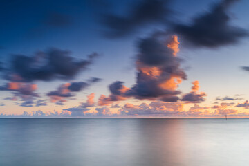 Moving clouds above large lake with smooth water and a sunset view from the coast