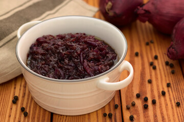 Red onion relish homemade with balsamic vinegar and brown sugar in a white ceramic dish standing on a wooden background.