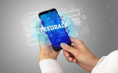 Female hand typing on smartphone with FEEDBACK inscription, social media concept