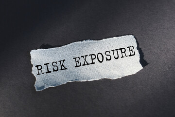 RISK EXPOSURE - text on torn paper on dark desk in sunlight.