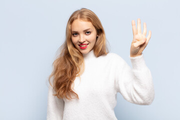 blonde woman smiling and looking friendly, showing number four or fourth with hand forward,...