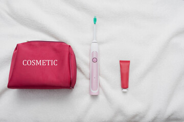 Cosmetic bag, ultrasonic electric toothbrush and tube of toothpaste, white background. Concept of oral care and healthy teeth by using ultrasonic smart toothbrush