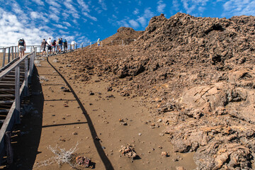 Tourists hike to a viewpoint on the volcanic cinder of Bartolome island in Galapagos National Park. Different formations of volcanic geology, spatter and tuff cones, lava flows and lava tubes