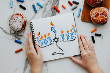 A girl drawing a celebration card with menorah (traditional candelabra) and candles for Happy...