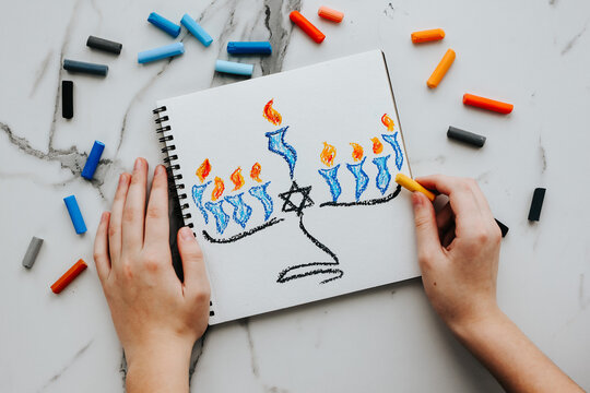 A girl drawing a celebration card with menorah (traditional candelabra) and candles for Happy Hanukkah jewish holiday. 
