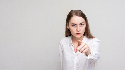 Portrait of a angry young woman pointing finger at you camera gesture, white background, 16:9