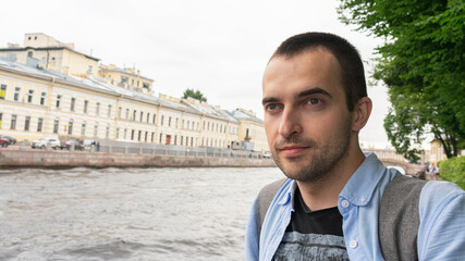 Man traveling in Saint Petersburg, guy with a beard looks away, city landscape with a river, portrait, 16: 9
