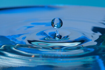 Amazing shot of a droplet bouncing on water -  blue background