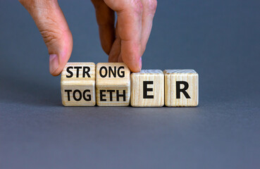 Stronger together symbol. Businessman turns cubes and changes the word together to stronger. Beautiful grey background, copy space. Business, motivational and stronger together concept. - obrazy, fototapety, plakaty
