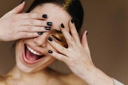 Carefree young woman with party makeup expressing happiness. Studio photo of inspired brunette girl laughing on dark background.