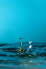 Amazing vertical shot of a droplet bouncing on water -  blue background