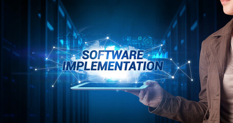 Young business person working on tablet and shows the inscription: SOFTWARE IMPLEMENTATION