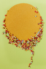Creative concept made with smarties candy in a shape of sunny golden baloon on a pastel green background.