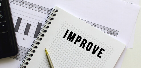 Text IMPROVE on the page of a notepad lying on financial charts on the office desk.