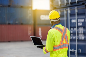 worker man in protective safety jumpsuit uniform with yellow hardhat and use laptop check container at cargo shipping warehouse. transportation import,export logistic industrial service