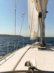 Fototapeta premium Yacht sailing away from the heads of Sydney Harbor, on a calm and sunny day. View from the boat's cockpit over into the horizon, with North Head in sight