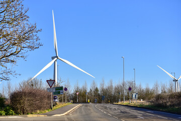 A road, and in the background a large wind turbine against a blue sky.