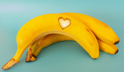 Bunch of bananas with heart shaped cut isolated on light blue background.