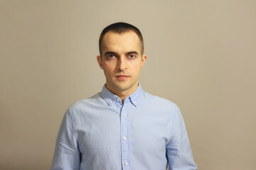 Serious man wears casual blue shirt, has serious expression, gray background, copy space