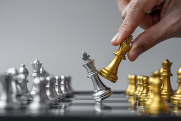 businessman hand moving gold Chess King figure and Checkmate enermy or opponent during chessboard...