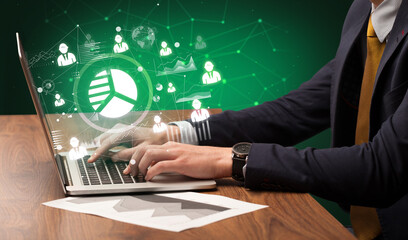 Business hand working on laptop with pie chart icons coming out from the screen, successful business concept