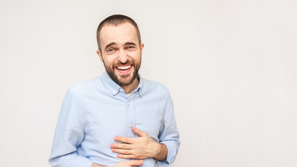 Laughing young man holding hands on stomach while laughing out loud at something joke. Concept of positive people emotions, white background, 16:9, copy space