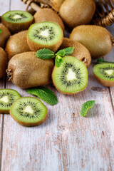 Ripe raw kiwi green whole and slices falling from basket with mint leaves
