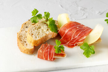 Traditional spanish jamon slices (dried pork meat) with melon and fresh herbs on marble board