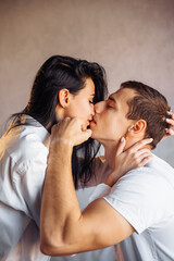 Attractive, young couple of lovers having sex at home in the bed in bright room. Girl kissing her boyfriend oddly, gently pulling back his lower lip. Celebrating Valentine's Day - February 14