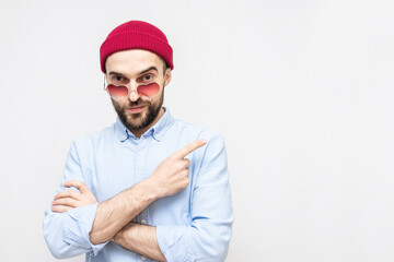 Bearded man points to a copy of the space, a man in love wears heart-shaped glasses, portrait, white background