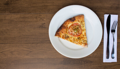 A delicious slice of mozzarella cheese pizza with slices of red tomatoes, served on a plate. Cutlery ready to be used. Gastronomic photography with space for texts on the left.
