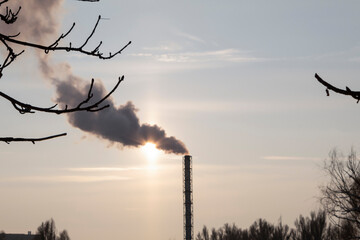 Thick smoke comes from the factory chimney, through which the sun shines.
