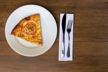 A delicious slice of mozzarella cheese pizza with slices of red tomatoes, served on a plate. Cutlery ready to be used. Gastronomic photography with space for texts.