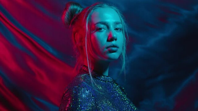 Cool young teen girl in futuristic dress with two buns hairs on moving waving background in colorful neon light
