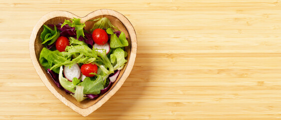 vegetable salad of fresh and greens in wooden bowl heart on wooden background, Healthy food, top view horizontal. copy space banner.