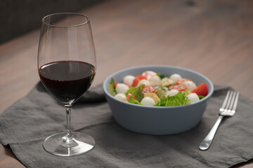 Glass of red wine with salad with romaine, tomatoes and mozzarella in blue bowl