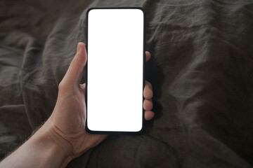 man hand holding phone with white screen over bed on background