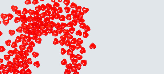 A lot of red little glass hearts lie scattering on a gray background, a wide horizontal banner, a soft focus, a place for text, concept of valentine's day