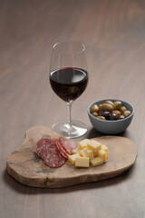 olives, salami and vintage cheese with glass of red wine on walnut table
