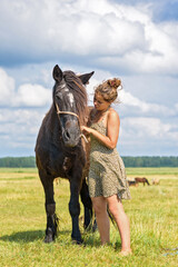 A young beautiful girl puts a halter on a horse on the field.