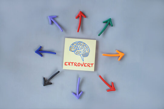 Extrovert and brain written on yellow sticky note and colorful arrow on grey background. Outgoing person concept and personality idea