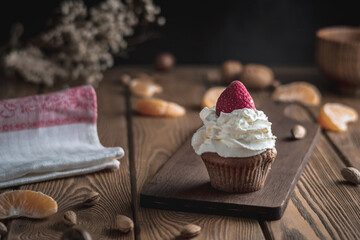 Delicious cupcake with whipped cream and strawberry topping on a rustic wooden table