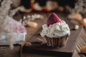 Delicious cupcake with whipped cream and strawberry topping on a rustic wooden table